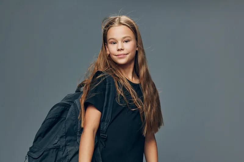 Girl with long hair and black backpack posing in casual clothes on grey background for education, school, youth and lifestyle concept with confident expression and natural look.