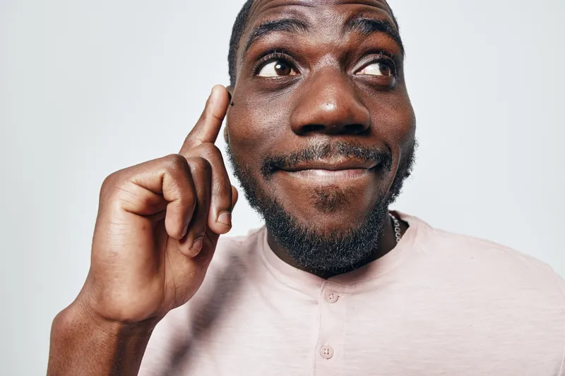 African American man with dark skin pointing finger to head thinking and smiling in casual shirt on white background. Portrait, emotion and idea concept with positive expression.