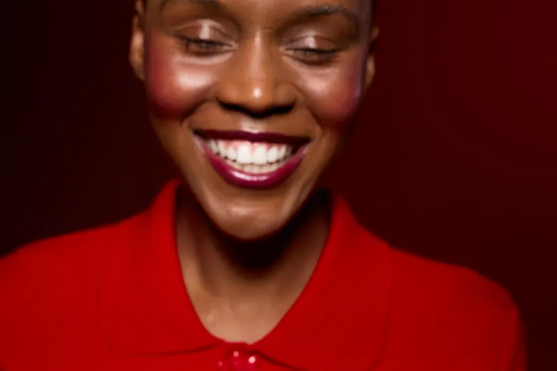 Close-up of happy African woman with dark skin smiling with eyes closed wearing red shirt. Concept of joy, happiness, beauty, and positive emotion on red background in studio lighting.