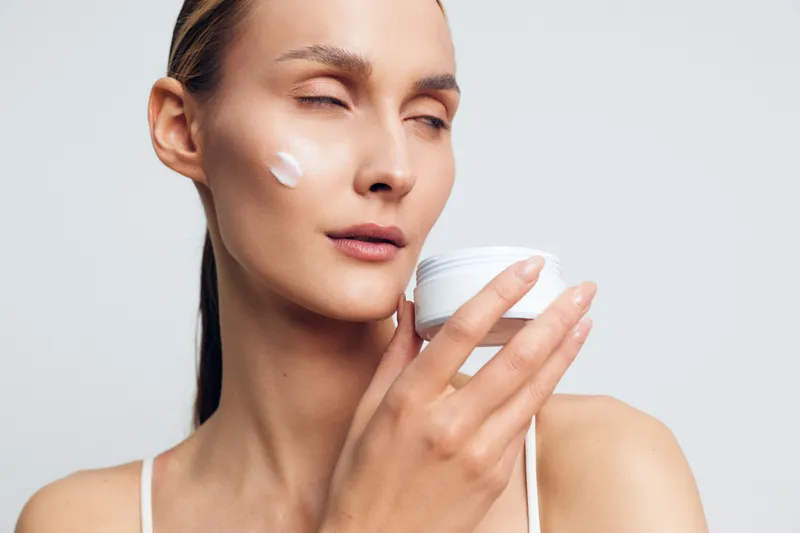 Woman skincare cream moisturizer on face, beauty portrait, calm hygiene in spa relaxation, light background, smooth skin texture, soft daylight, closeup beauty care