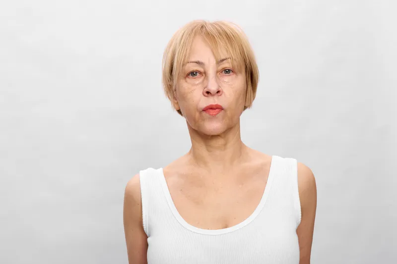 Woman portrait in studio, blonde adult with neutral expression, closeup face against white background, shoulders visible, soft lighting, clean minimal look, calm personal identity