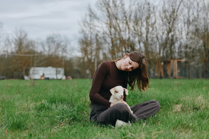 Young woman sits on grass with a dog in an open park, sharing a gentle moment outdoors. Emphasis on lifestyle, companionship, nature, and wellbeing with soft natural lighting.