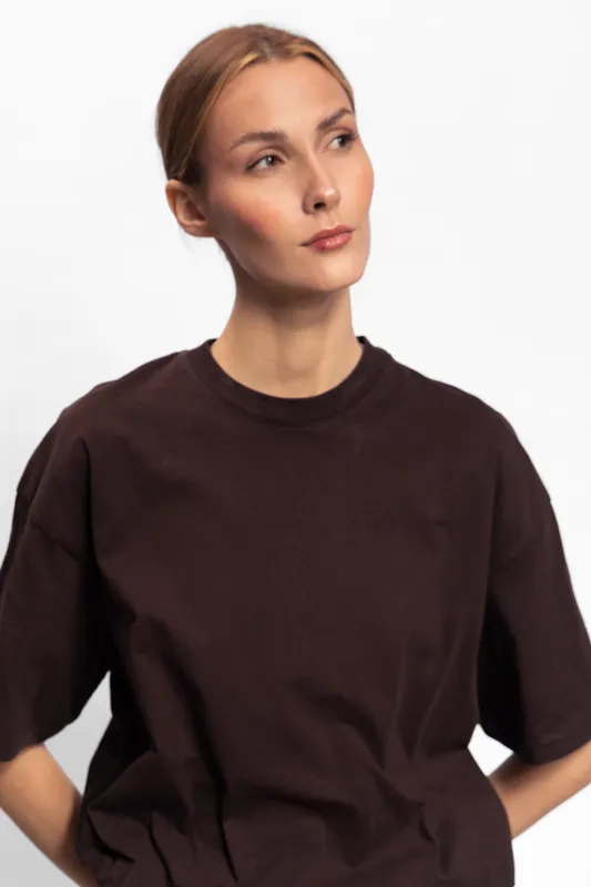 Young woman with light skin and blonde hair wearing a dark brown t shirt looks thoughtfully to the side on a white background. Portrait with natural light and minimal styling.