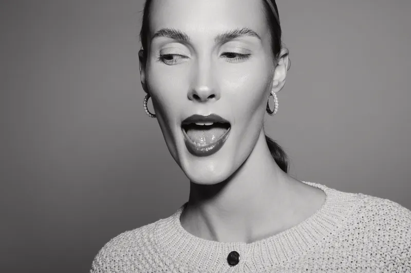 Portrait of a light skinned caucasian woman with slicked back hair making a playful face. Studio shot in black and white with minimalistic background. Concept of fun and expression.
