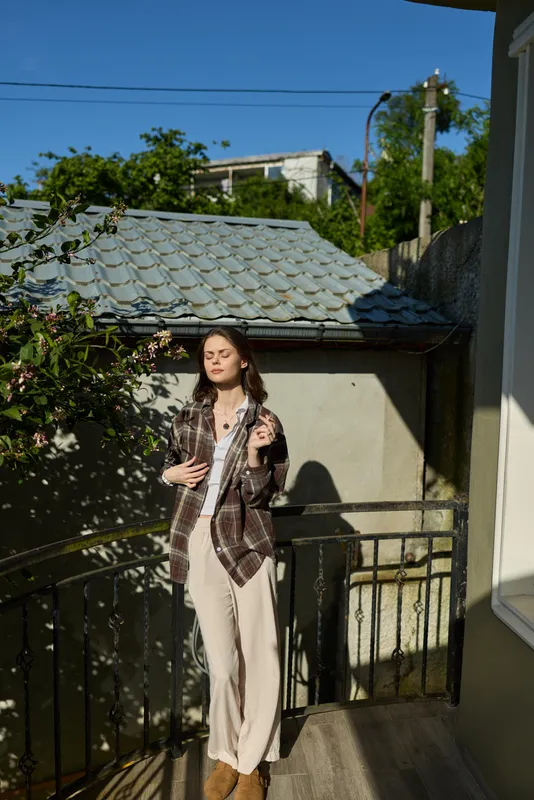Woman lifestyle on a sunlit balcony, casual chic outfit, relaxed pose, modern terrace setting with railing, showcasing everyday fashion and serene confidence in natural light