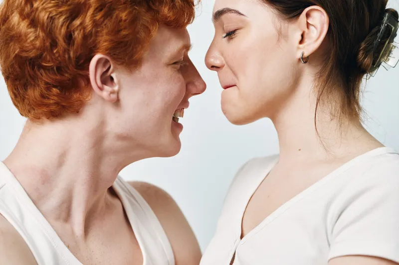 Young couple standing close with noses touching in playful intimate moment against plain background. Smiling man and woman showing affection and tenderness indoors.