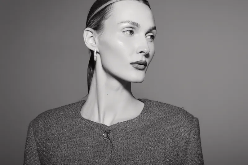 Elegant white woman with pale skin and slicked back hair looks sideways wearing textured jacket in studio. Fashion portrait with soft lighting.