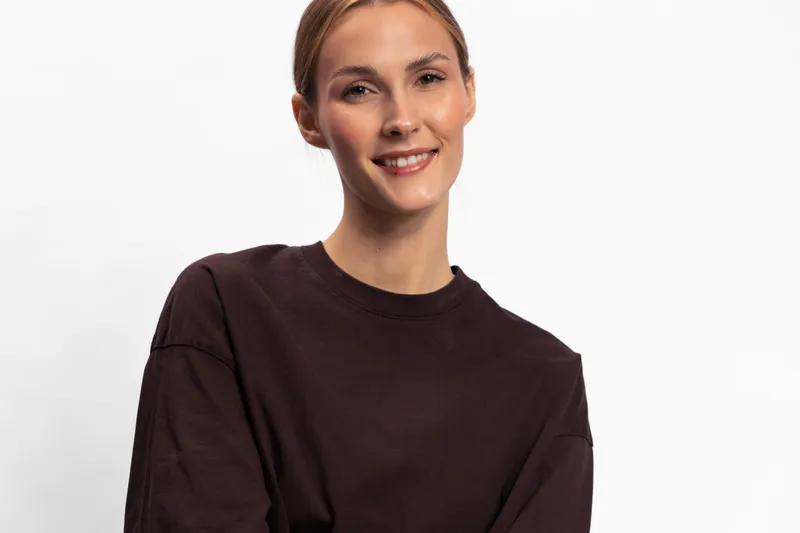 Smiling young woman with light brown hair wearing dark casual sweater poses against white background. The portrait shows natural beauty, confidence, and positive mood in studio lighting.