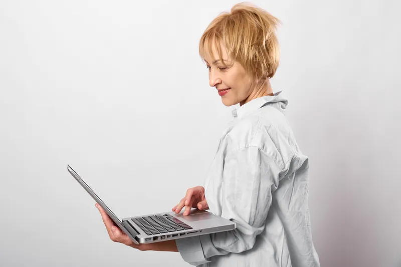 Woman laptop typing in studio white profile focused communication technology work, female indoors, calm expression, keyboard screen, blank background