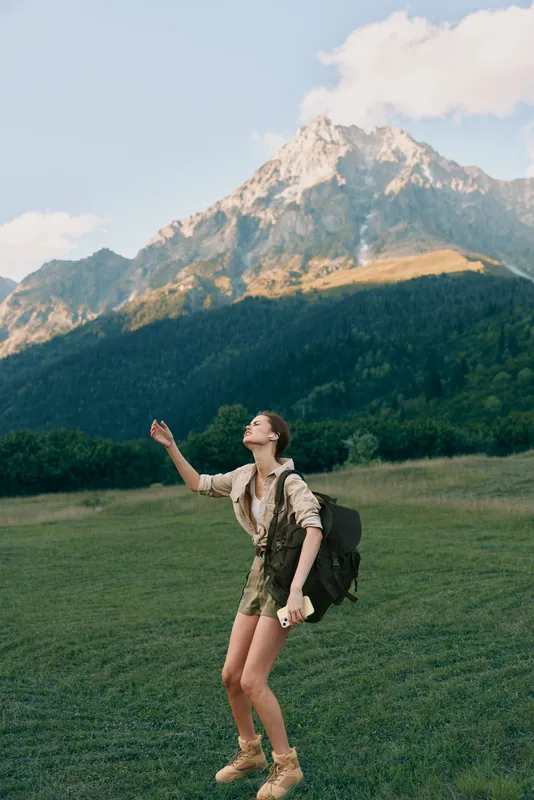 Woman hiking in a field with a backpack, gazing at distant mountains under clear skies. Outdoor nature, adventure, and wellness, with warm, inviting light.