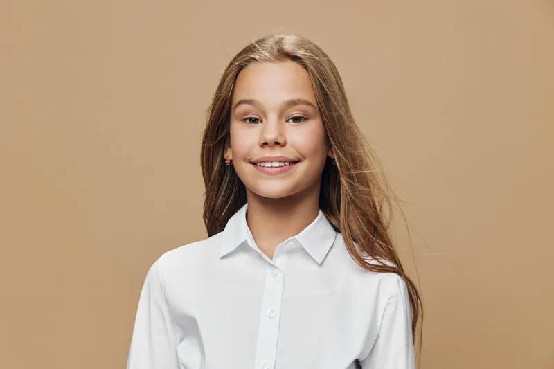 Girl portrait smiling with long hair and white shirt standing on brown background. Teenager with natural look and casual style for youth, happiness, beauty and lifestyle.