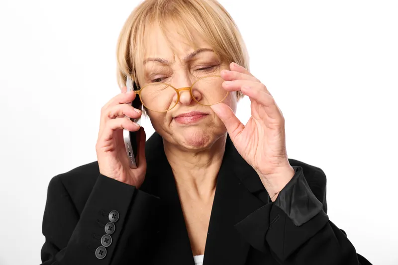 Elderly woman portrait, smartphone calling, glasses adjusted with worried expression, business attire, studio white background, soft light, clean close view