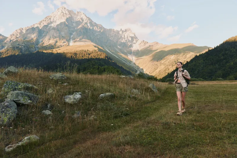 Active woman hiking in nature, walking on grassy meadow, mountain landscape background, casual outfit, sunny day, healthy lifestyle, outdoor adventure