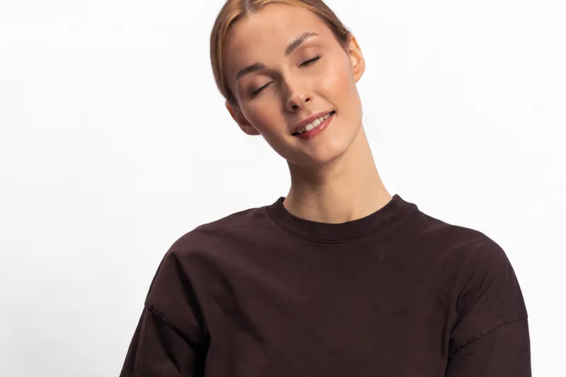 Young woman with closed eyes and gentle smile wearing dark sweater on white background. Concept of calm, relaxation, peacefulness, and natural beauty in studio portrait.