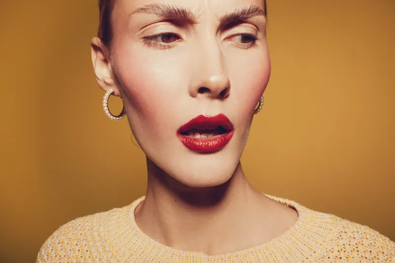 Close-up of a woman with red lipstick and hoop earrings looking to the side on a yellow background. Concept of fashion, beauty, makeup, and portrait photography.