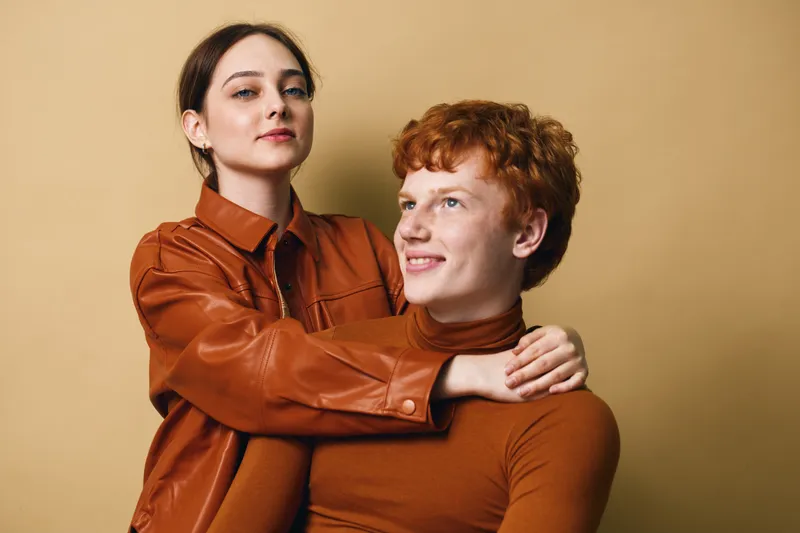 Couple, young woman and man, posing with warm expressions for friendship and relationship, casual clothing in cozy studio with soft beige background.