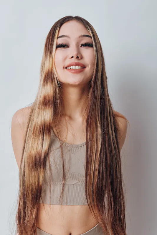Young woman with long straight hair and natural makeup smiling in neutral tank top against white background for beauty, fashion and lifestyle concept.