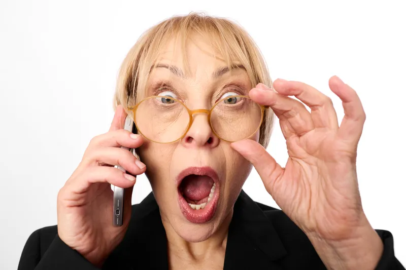Woman, surprised, glasses, phone, calling, shocked expression, blonde businesswoman holds smartphone near ear, raises hand to adjust glasses, open mouth portrait, studio close shot, white background