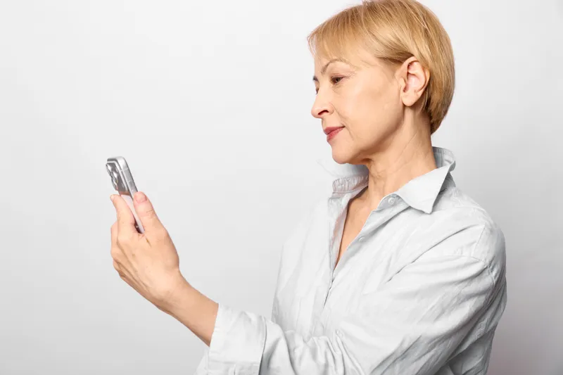 Woman smartphone mobile communication profile portrait blond studio white technology holding smartphone in hand, focused expression, using device on studio background, isolated