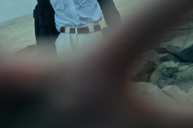 Beach scene with a man in a light shirt and white pants standing by rocks with a backpack, suggesting travel, exploration and casual mood