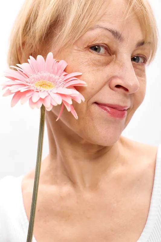 Smiling woman holding pink gerbera flower, close up portrait, soft white background, natural beauty and skincare concept, calm wellness mood with studio soft light