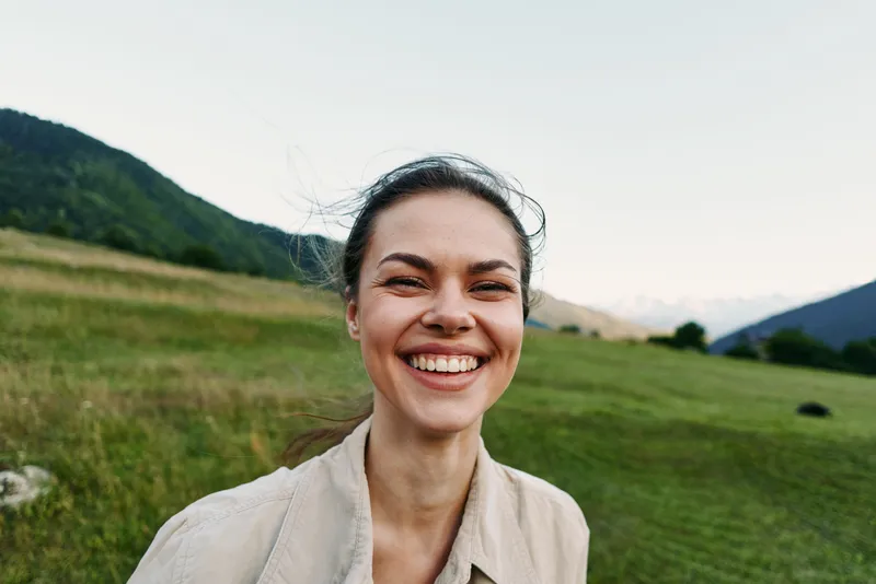 Smiling woman outdoors enjoying nature, close crop over a grassy field with hills, conveying wellness and lifestyle through warm natural light.
