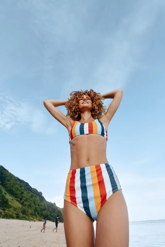 Woman, curly hair, swimsuit, striped, sea, sky, outdoors, sunny summer moment, arms behind head, relaxed pose, looking up, ocean horizon, distant coastline, natural light