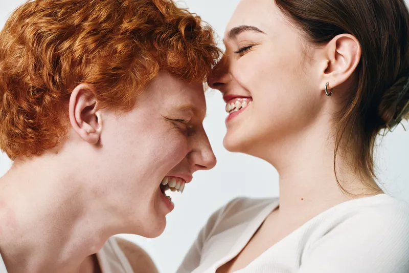 Couple smiling and close together with affection, young man and woman showing happiness and love in casual clothing on white background. Emotion and connection.