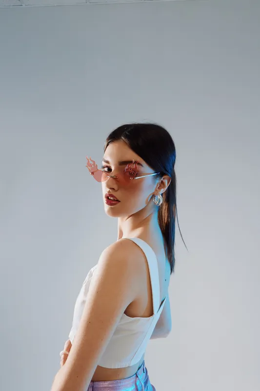 Young woman in stylish sunglasses poses confidently in a white top against a neutral background. Concept of beauty, fashion, and modern style in portrait photography.