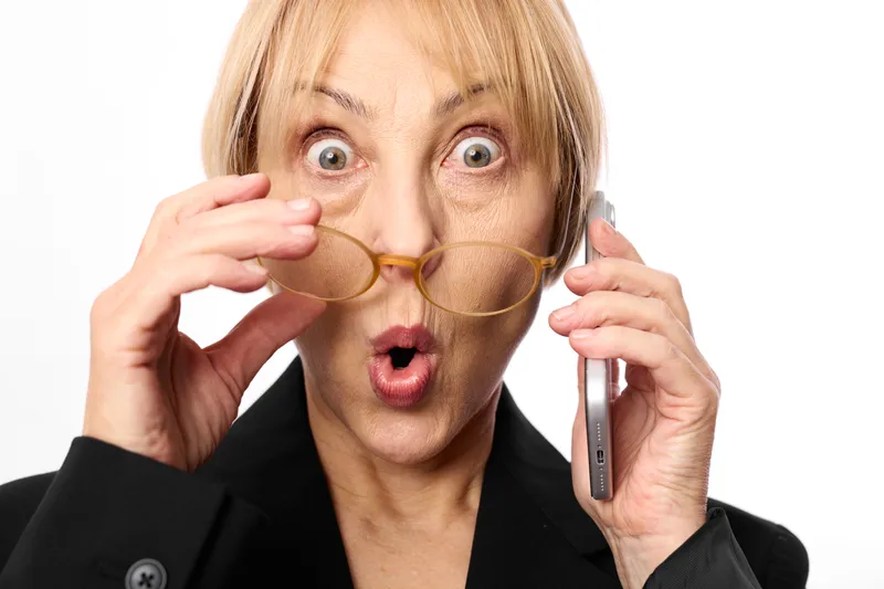 Surprised woman in suit with stethoscope headset, holding eyeglasses and phone receiver, wide open mouth, telehealth concept for urgent communication and stress
