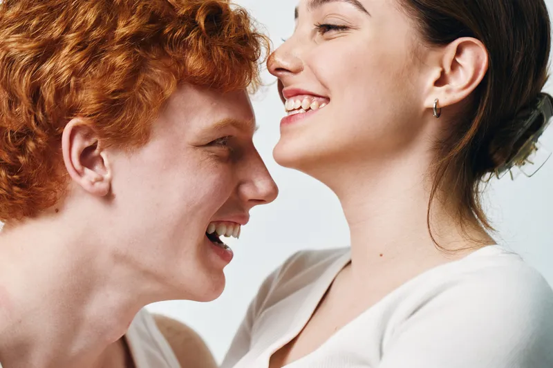 Young couple smiling and laughing together with close intimacy and happiness on white background. Portrait of redhead male and brunette female showing joy and affection.