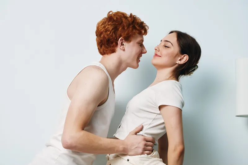 Young couple, man and woman smiling with affection, embracing and looking at each other, casual clothing, love and relationship, indoors on white background for connection and happiness.