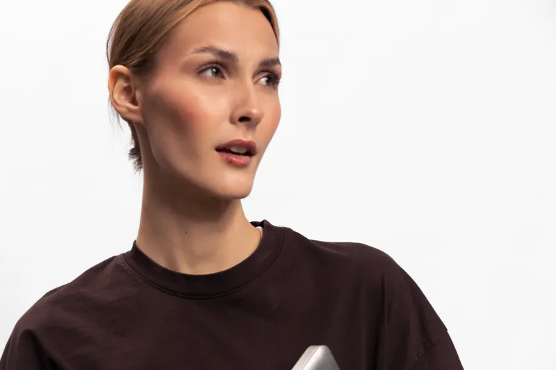 Young woman with short hair wearing a dark shirt looks aside with an interested expression. Minimalistic studio portrait on a white background with soft lighting.