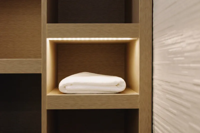 Towel neatly folded on a wooden shelf niche, clean and minimalist bathroom storage, warm wood tones and soft fabric create calm, organized home interior scene.