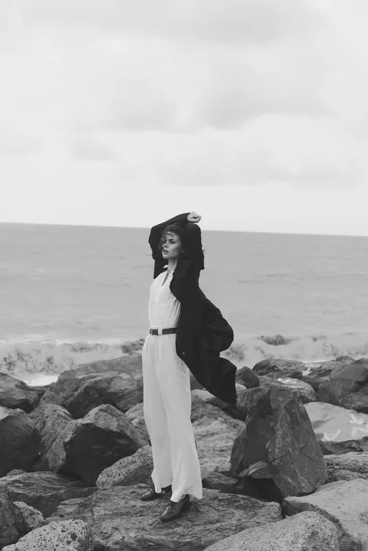 fashion woman sea rocks dress coat pose freedom horizon outdoor a monochrome scene capturing movement and elegance on a windy shore