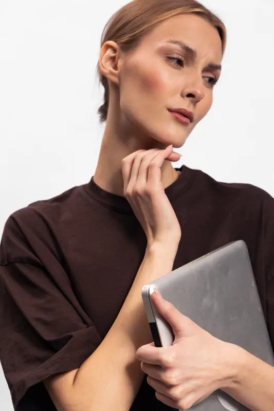 Young woman with short hair holds laptop close to chest, wearing casual dark t shirt. Studio portrait on white background. Concept of technology, work, and modern lifestyle.