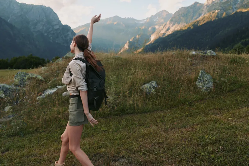 Young woman with backpack hiking in mountains during daytime. She enjoys nature, adventure, and outdoor lifestyle with casual clothing and natural scenery around.