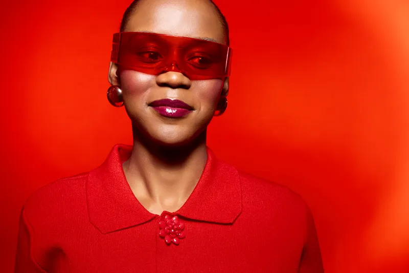 Portrait of a confident black woman with dark skin wearing red sunglasses and a red blouse against a bright red background. Concept of fashion, style, and bold color contrast.