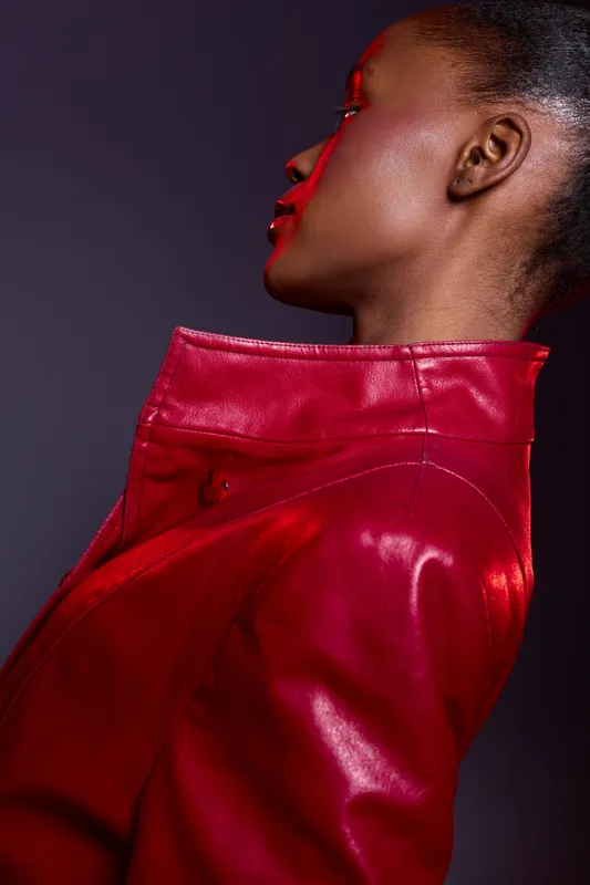 Profile of a dark skinned African woman wearing a red leather jacket against a dark background. Concept of fashion, style, elegance, and modern urban look.