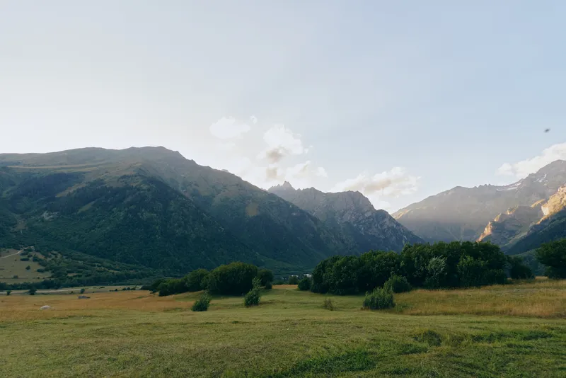 Mountain landscape opens to a vast valley with a grass field under a blue sky, offering a calm, expansive landscape that invites exploration.