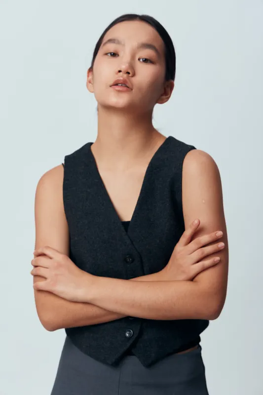 Portrait of confident woman with crossed arms wearing black vest against plain background. Serious expression, straight hair, modern style, studio lighting, minimalistic fashion look.