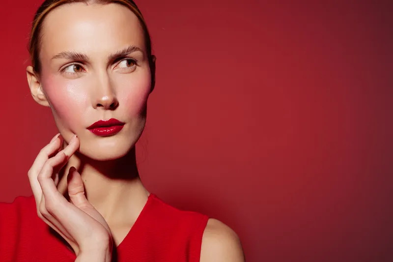 Portrait of a thoughtful woman with red lipstick and red dress on red background. Concept of beauty, fashion, makeup, and elegance with soft lighting and minimalistic style.