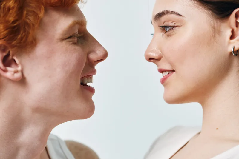 Portrait of two young people facing each other smiling. Closeup of man and woman with candid expressions against light background in casual style and natural look.
