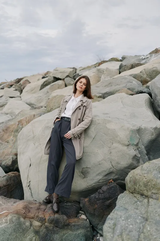 Young woman in casual outfit stands relaxed on large rocks outdoors under cloudy sky. Concept of fashion, nature, leisure, confidence, and autumn style in natural environment.