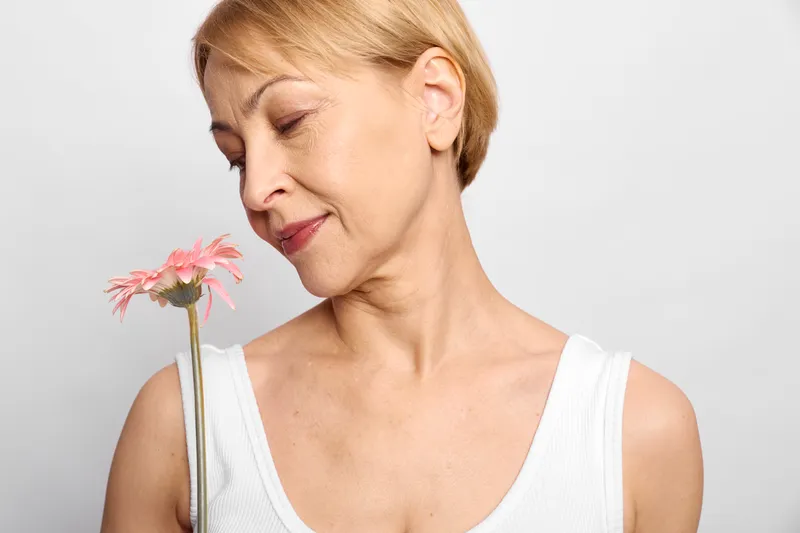 Woman blonde portrait holding flower on white background, eyes closed, thoughtful sadness, soft natural light, minimal closeup, sleeveless top, quiet mood, space