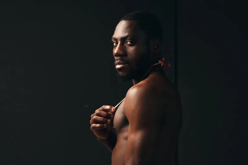 Creative visual designer style portrait of African American man with dark skin looking at camera with confident expression and muscular body on black background.