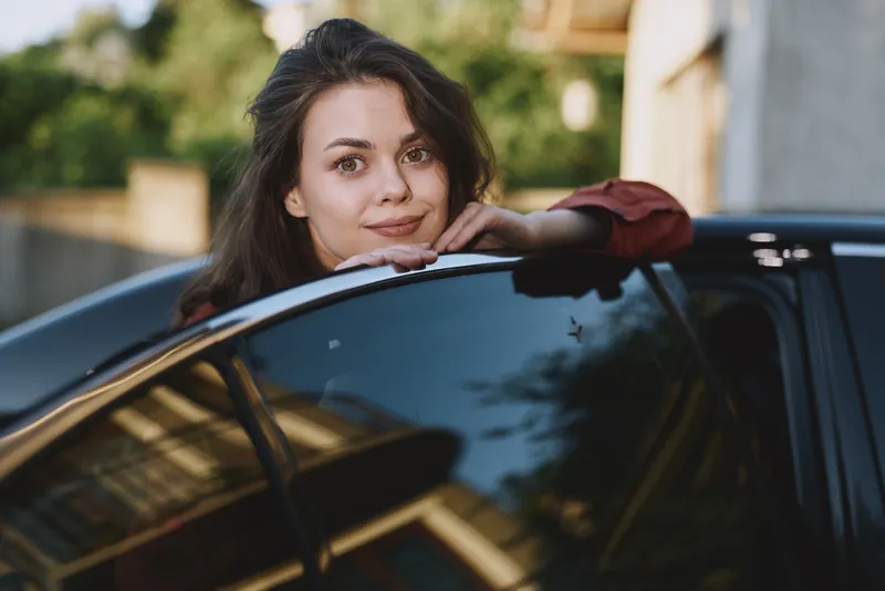 A woman lifestyle car leaning outdoor urban portrait casual relaxed daytime in a bright setting, capturing a candid moment of everyday confidence and calm