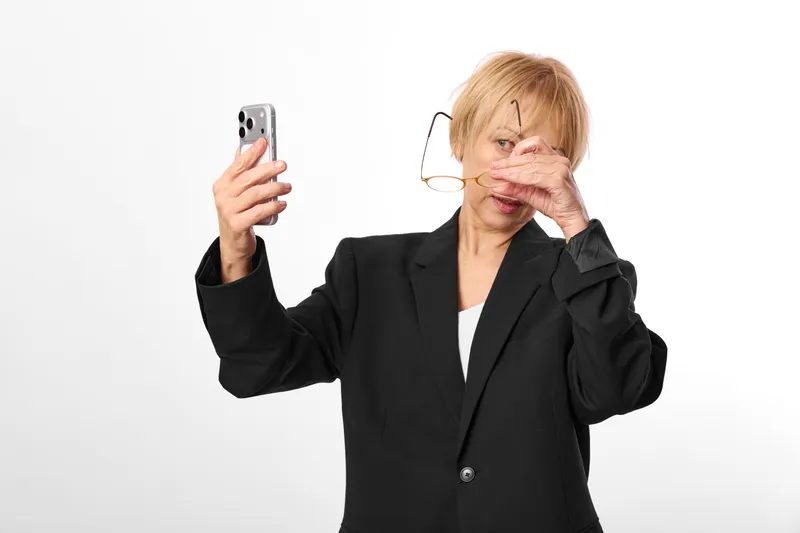Woman using smartphone while covering her face, showing stress and frustration, close up on a white studio background, business portrait with anxious communication mood, modern technology