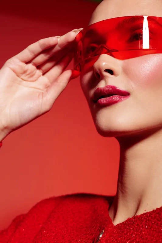 Close-up of a woman wearing red futuristic sunglasses and a red sweater against a red background. Concept of fashion, style, modern accessories, and bold colors.