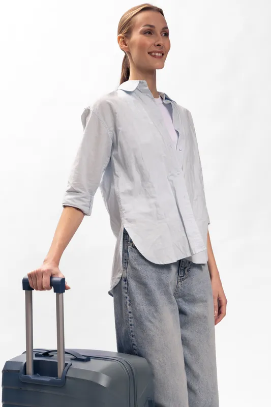 Young woman in casual clothes smiling, holding suitcase handle standing isolated on white background. Concept for travel, tourism, and vacation preparation with relaxed positive mood.